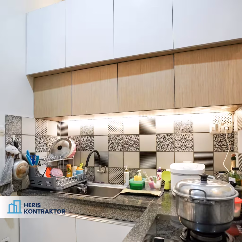 Dapur dengan area cuci, peralatan masak, dan bahan pembersih, serta backsplash motif kotak hitam putih yang menarik.