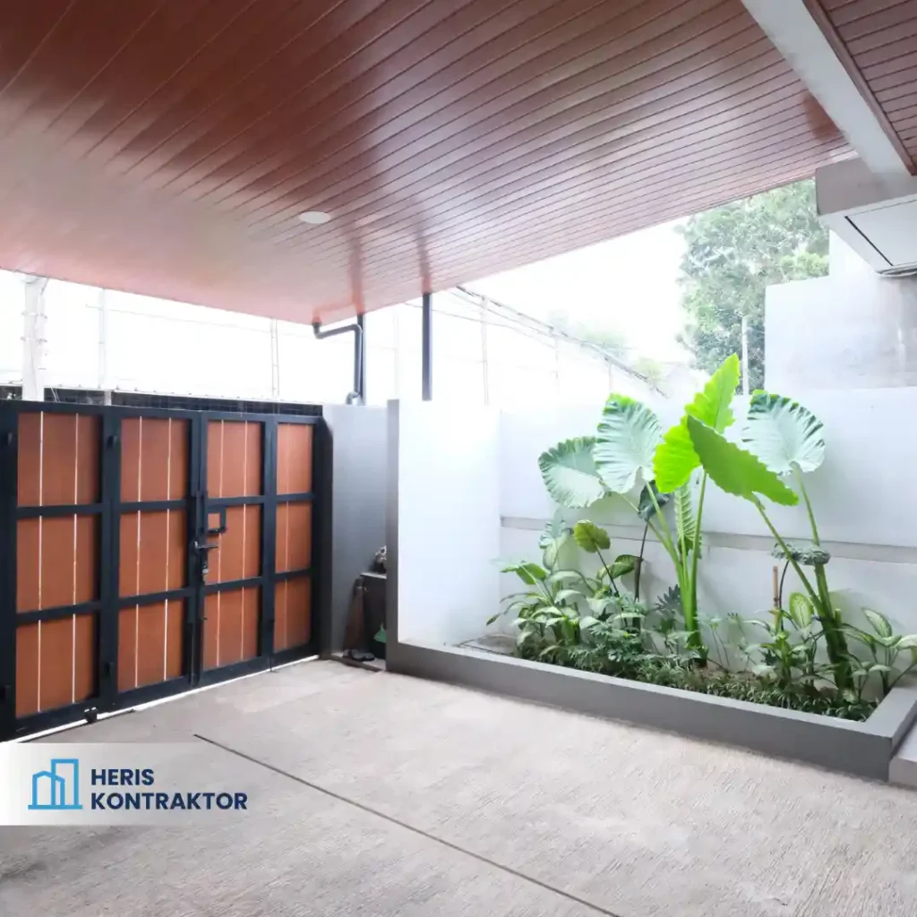 Carport dengan gerbang kayu dan tanaman hijau di area taman.