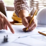Tangan yang menunjuk dan menggambar pada blueprint untuk pengajuan PBG.