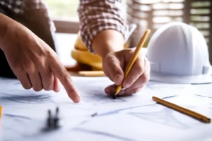Tangan yang menunjuk dan menggambar pada blueprint untuk pengajuan PBG.