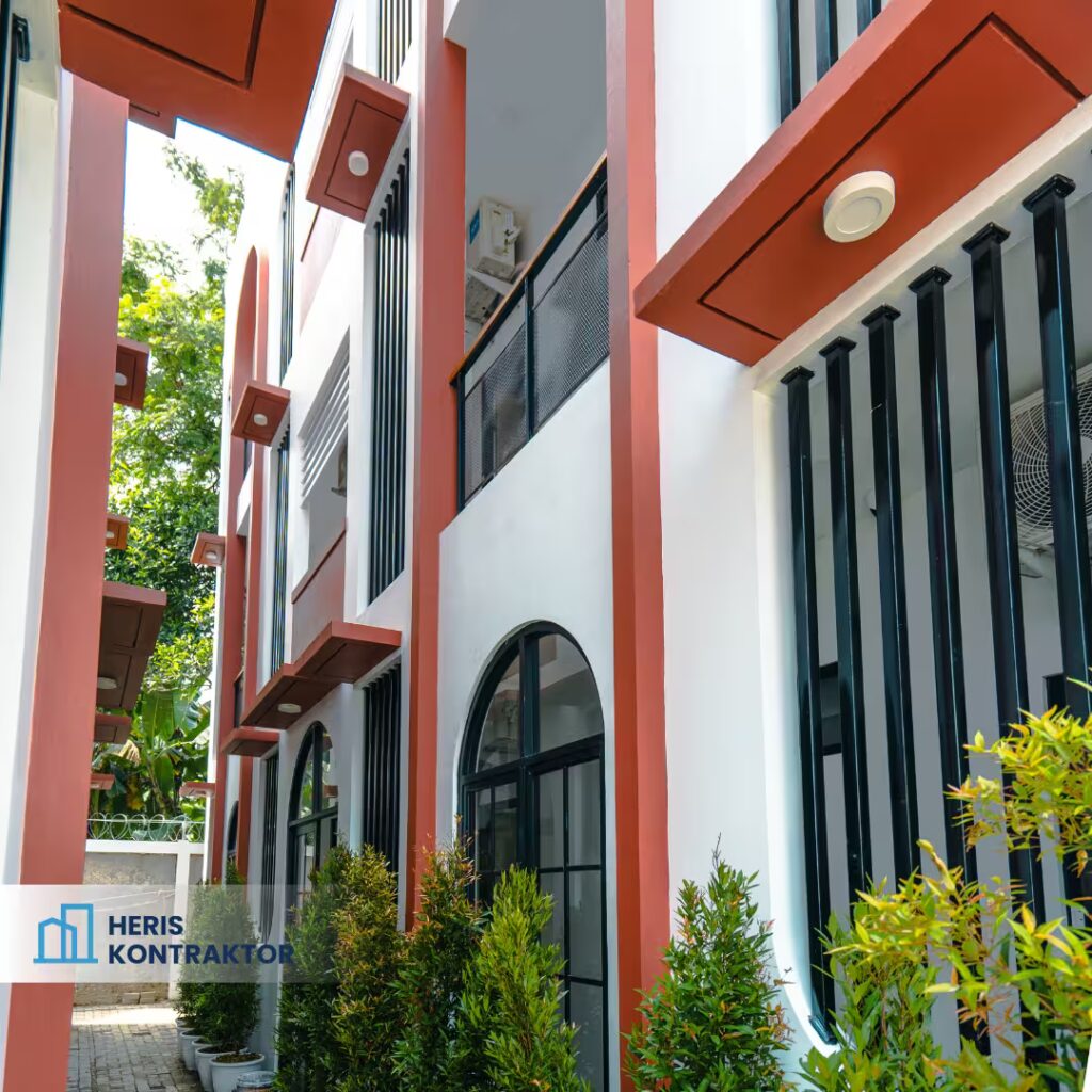 Koridor kost modern di Bogor dengan dinding putih, aksen merah, serta jendela lengkung hitam.