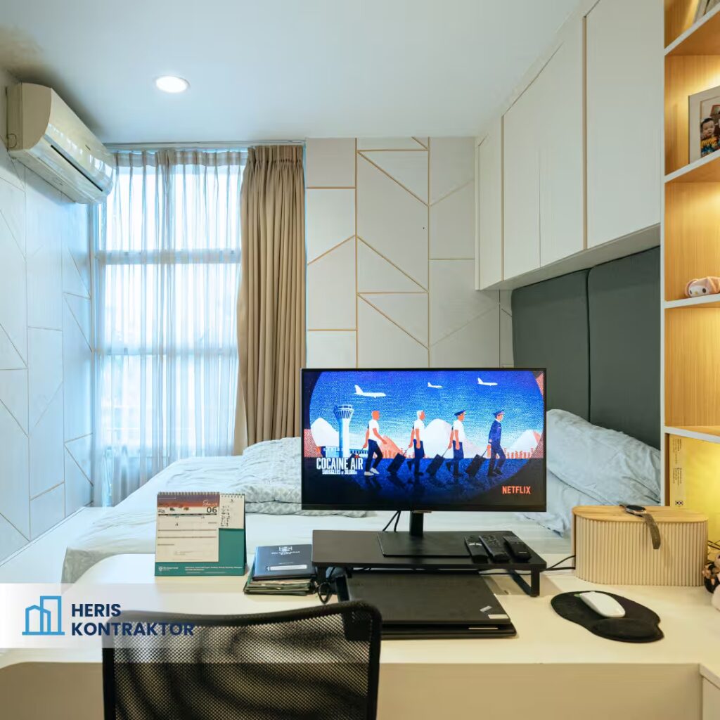 Interior kamar apartemen minimalis dengan tempat tidur, meja kerja, dan pencahayaan alami.