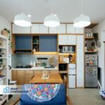 Tampak keseluruhan dapur modern minimalis dengan kabinet biru, meja makan kayu, dan tiga lampu gantung putih