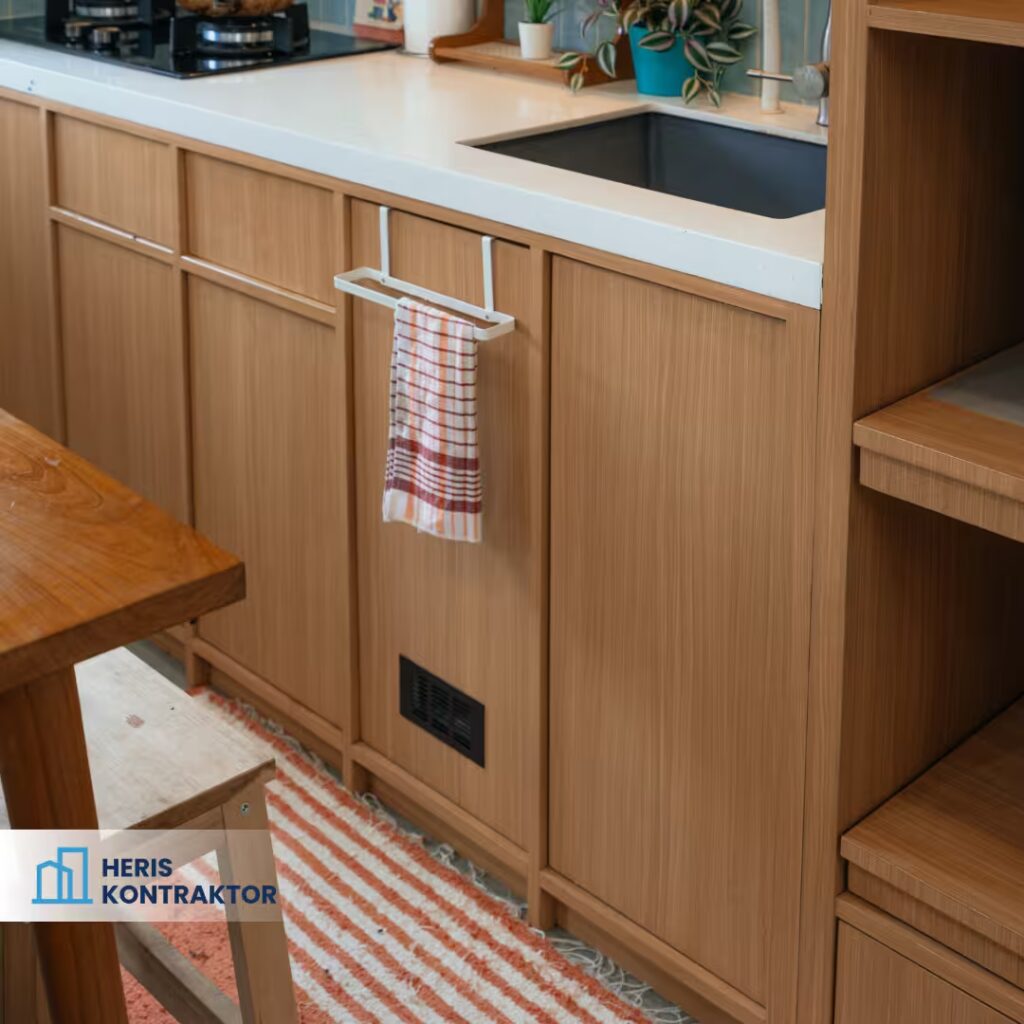 Detail kabinet bawah dapur finishing kayu natural dengan gantungan handuk putih dan meja makan kayu di samping